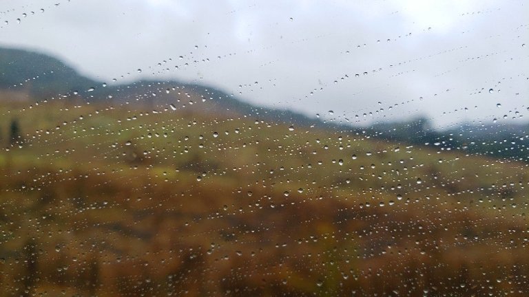 Raindrops across window, blurry hillside outside