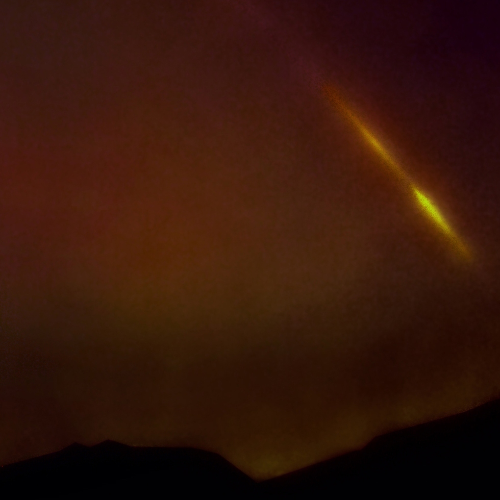 yellow tail of falcon 9 rocket streaks at about a 50 degree angle above Ojai hills, glowing red clouds below, black sky