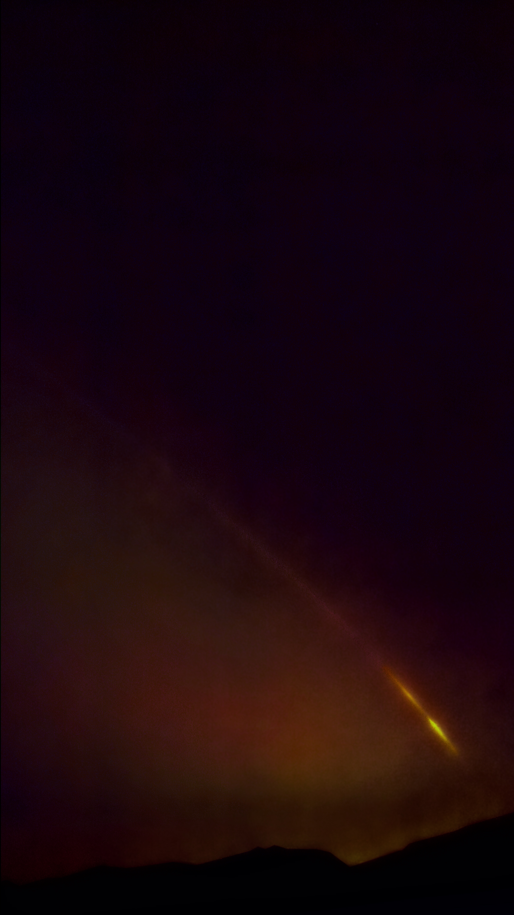 yellow tail of falcon 9 rocket streaks at about a 50 degree angle above Ojai hills, glowing red clouds below, black sky